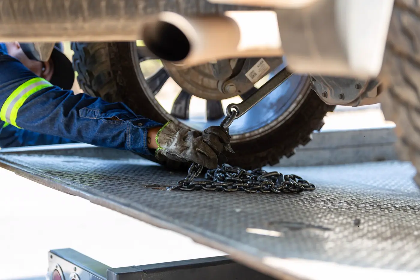 A gloved hand hooking a tow chain under a truck on a flatbed deck (representative photo)