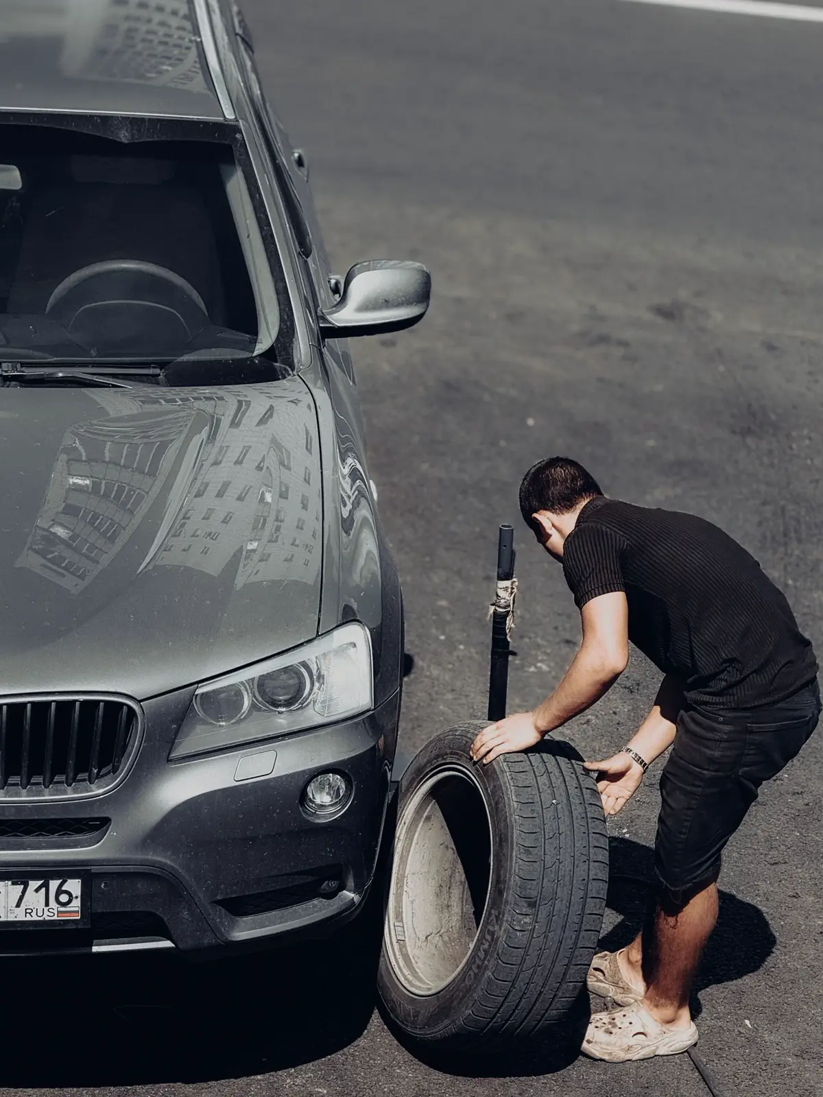 A man rolling a wheel into place beside an SUV (representative photo)